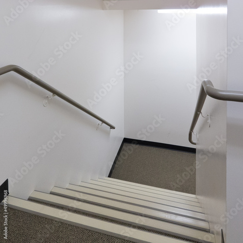 Looking down a well lit staircase with handrails photo
