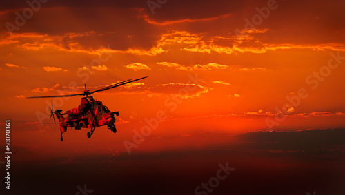 Military helicopter in flight against a dramatic red sky