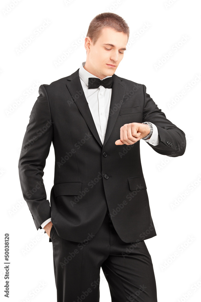 A young man in black suit with bow tie looking at wrist watch A young man in black suit with bow tie looking at wrist watch