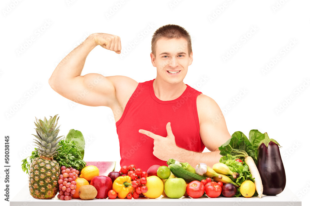 Fit young man showing his muscles behind a pile of fruits and ve Fit young man showing his muscles behind a pile of fruits and ve