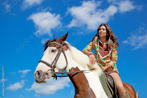 A young girl dressed as an Indian rides a paint horse. Focus on