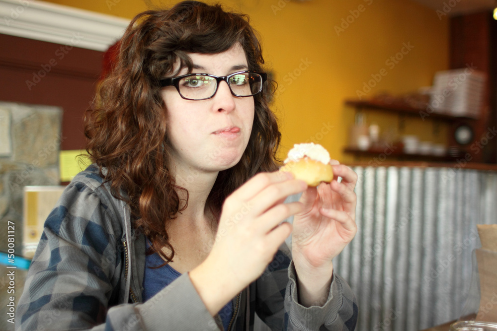 Young woman eating a cream puff at a cafe. Young woman eating a cream puff at a cafe.