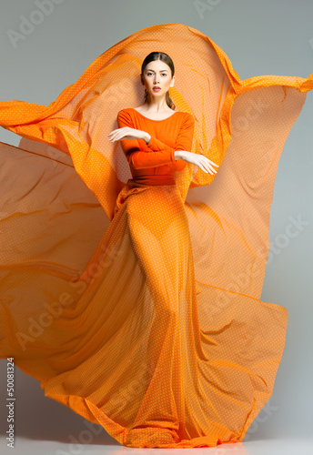 Leinwand Poster beautiful woman in long orange dress posing in the studio