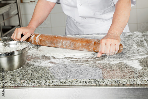 Female Chef Rolling Dough In Kitchen