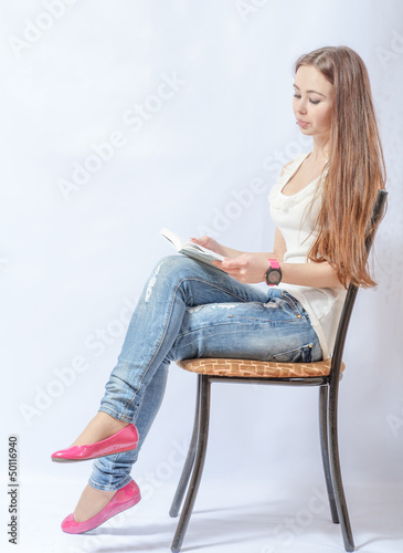 woman sitting on a chair in jeans reading a book
