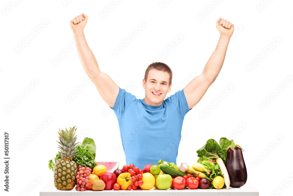 Excited guy gesturing happiness seated on a table full of fruits Excited guy gesturing happiness seated on a table full of fruits