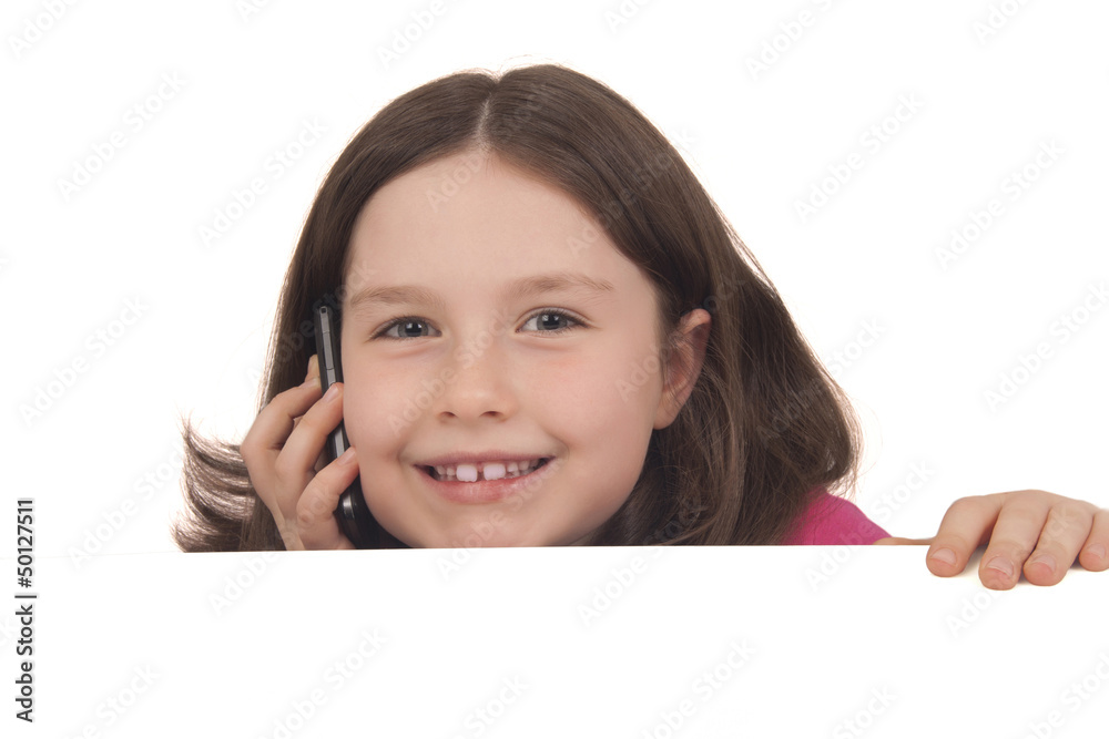 Beautiful little girl talking on a mobile phone behind copy spac