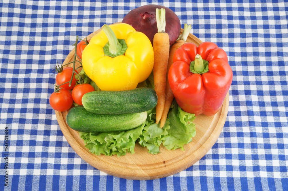 Vegetables on wooden cutting board on tablecloth Vegetables on wooden cutting board on tablecloth