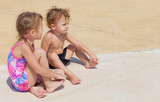 little girl and little boy sitting near the swimming  pool
