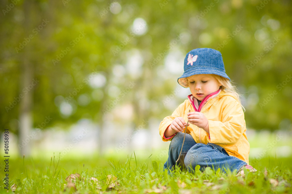 Adorable girl in hat play on grass with fallen leaves in park