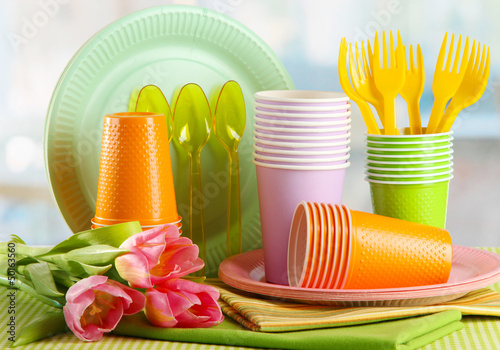 Fototapeta Naklejka Na Ścianę i Meble -  Multicolored plastic tableware on table with tulips close up