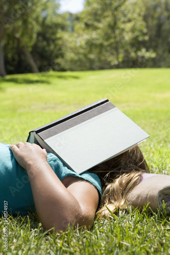 Girl sleeping in grass with book on her head photo