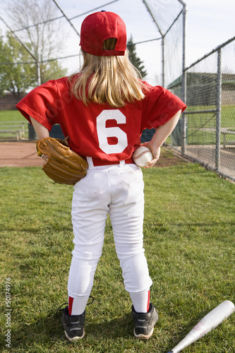 Girl in baseball uniform standing on field photo