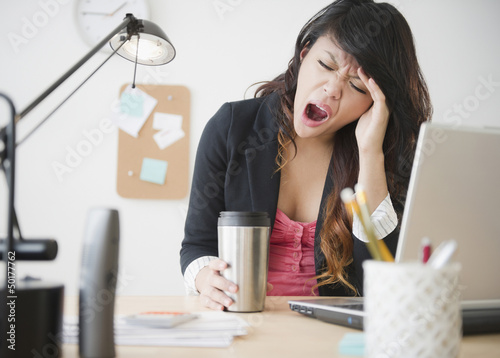 Pacific Islander businesswoman yawning at desk photo