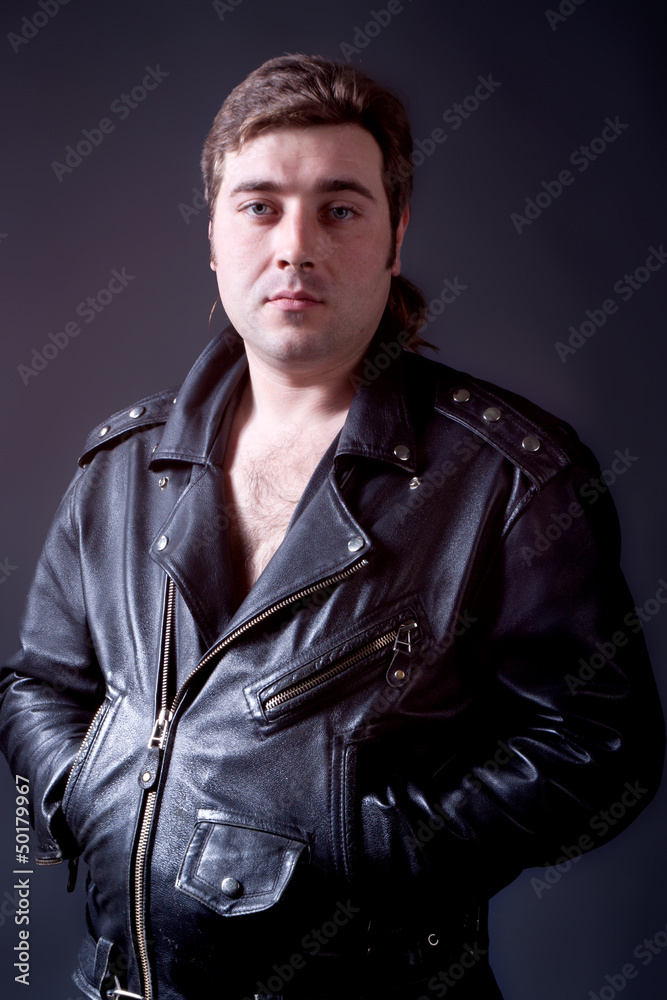 portrait of beautiful young man in a leather jacket on a gray ba