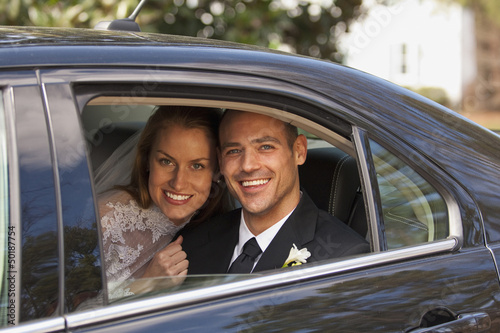 Caucasian bride and groom in back seat of car photo