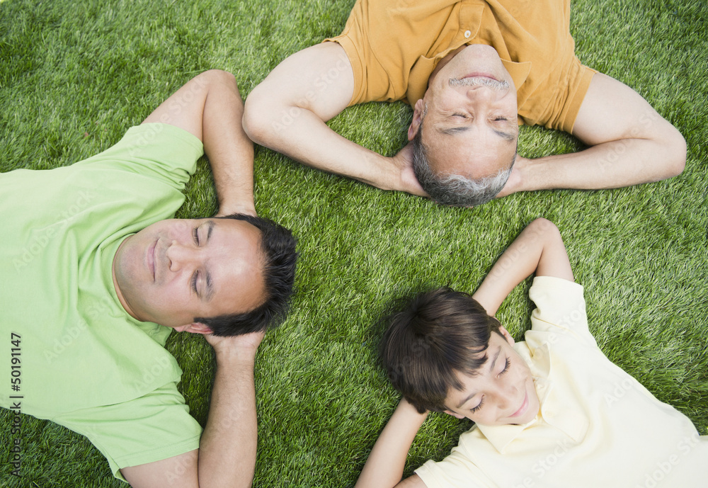 Hispanic grandfather, father and son laying in grass