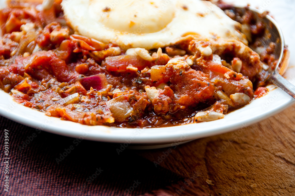 Stewed tomatoes and poached eggs in a bowl with a spoon Stewed tomatoes and poached eggs in a bowl with a spoon