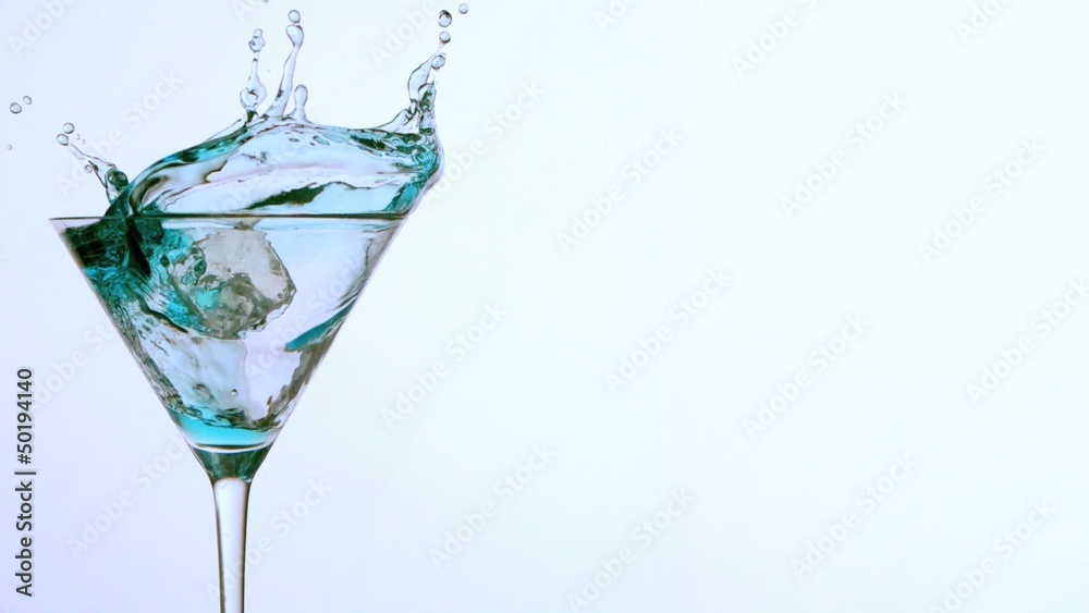 Ice falling into cocktail of blue alcohol on white background Ice falling into cocktail of blue alcohol on white background