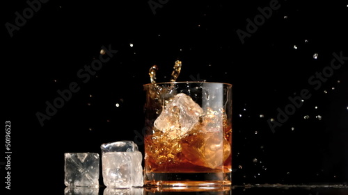 Ice cubes falling into glass of whiskey and ice