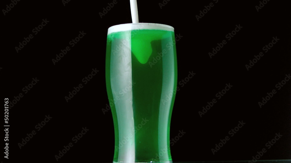Foam pouring onto pint of green beer on black background Foam pouring onto pint of green beer on black background