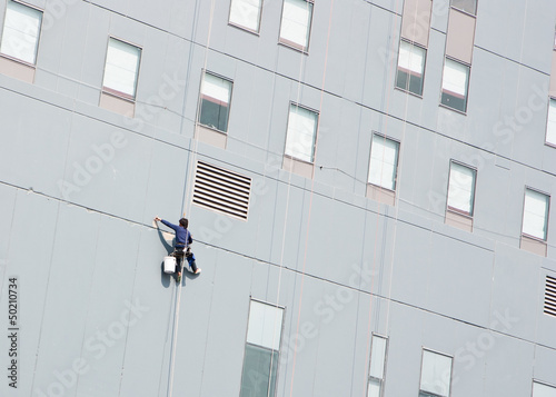 Asian man is plastering skyscraper facade with putty