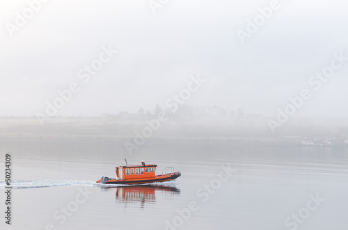 Smale lone orange boat sailing in mist