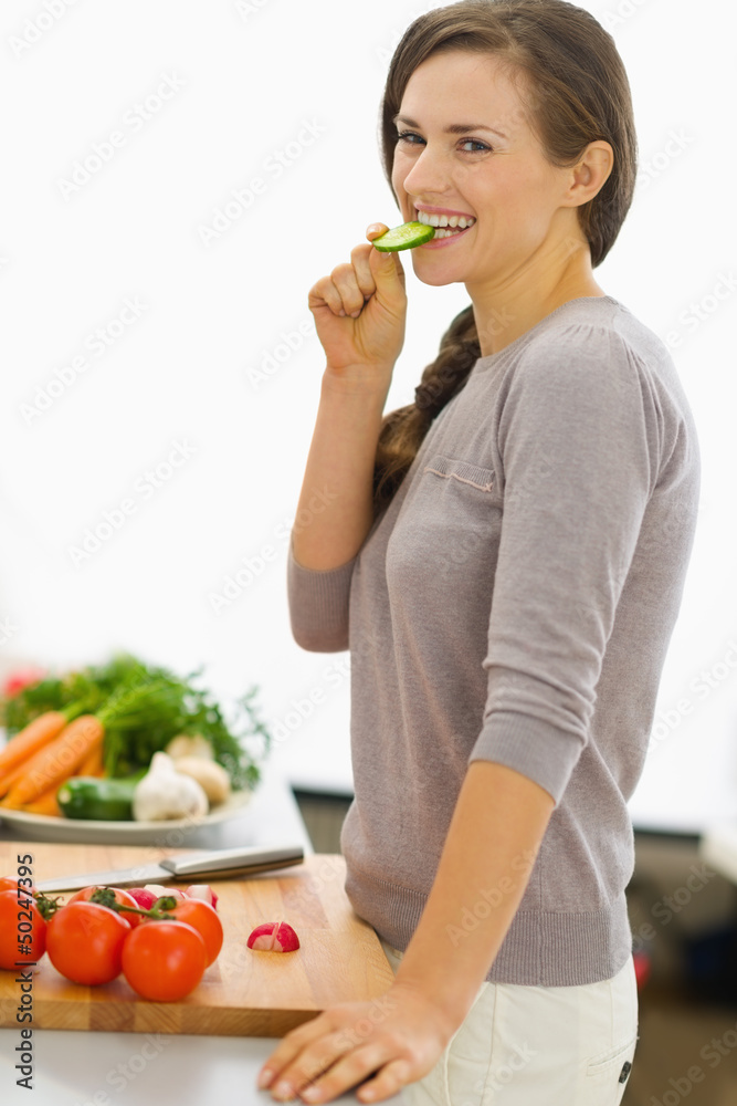 Happy young housewife tasting vegetables while preparing salad Happy young housewife tasting vegetables while preparing salad