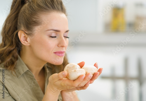 Young housewife smelling mushroom in kitchen