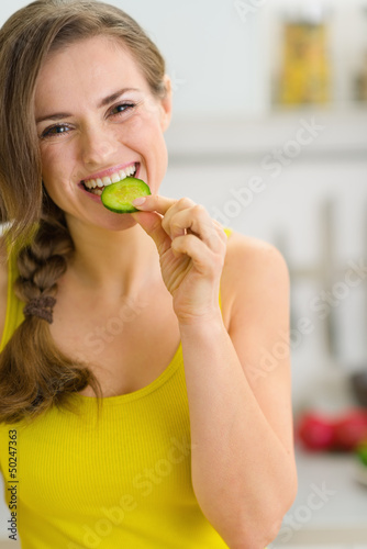 Smiling young woman eating slice of cucumber