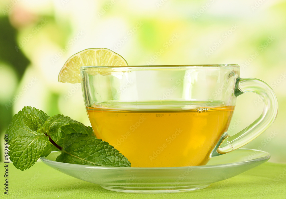 Cup of tea with mint on table on bright background