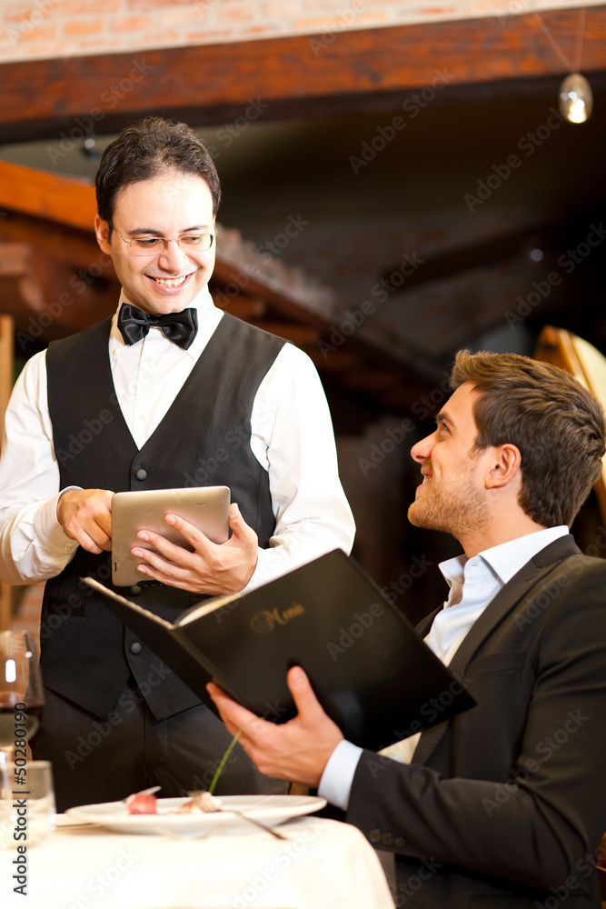 Young man at the restaurant ordering meal to a waiter