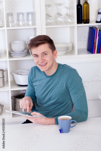 young man sitting with a tablet pc and tea cup in the kitchen