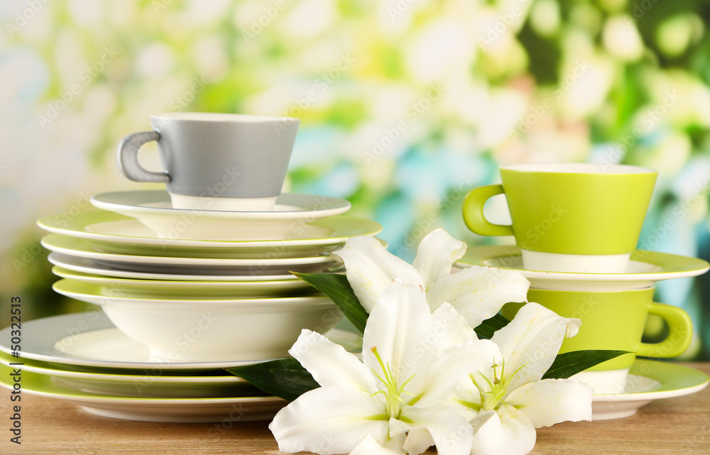 Empty plates and cups on wooden table on green background Empty plates and cups on wooden table on green background