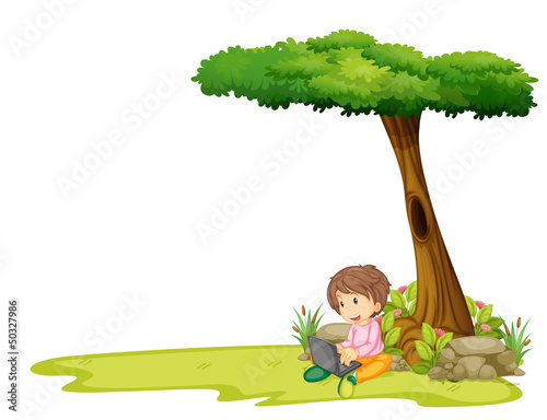 A boy with a laptop under a tree