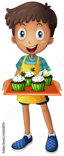 A young boy holding a tray with cupcakes
