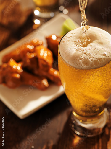 pouring beer with chicken wings in background.