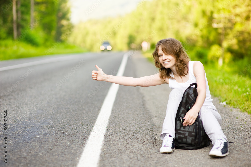 Pretty young woman hitchhiking along a road