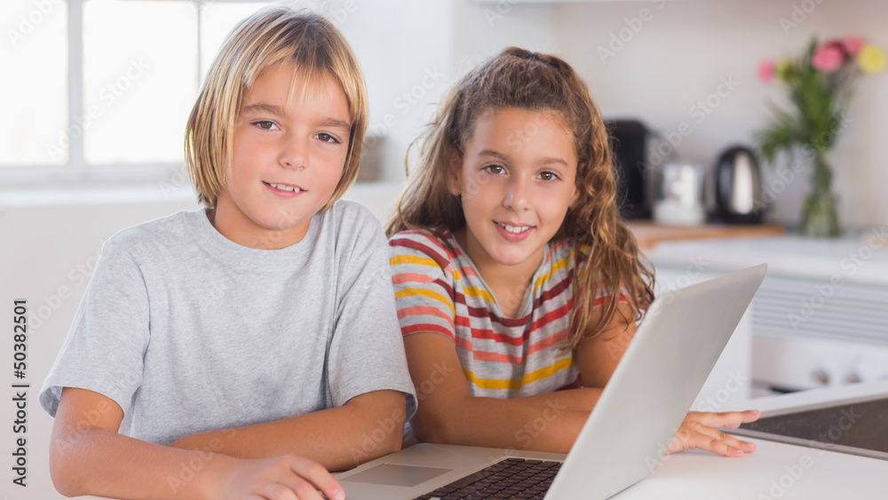 Two children looking at the camera together with laptop in front Two children looking at the camera together with laptop in front