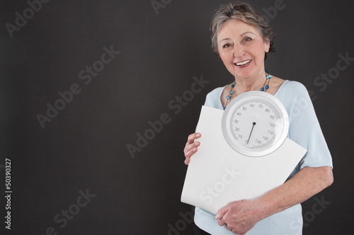 Älter Dame schaut auf ihre Figur - mit Waage in der Hand photo