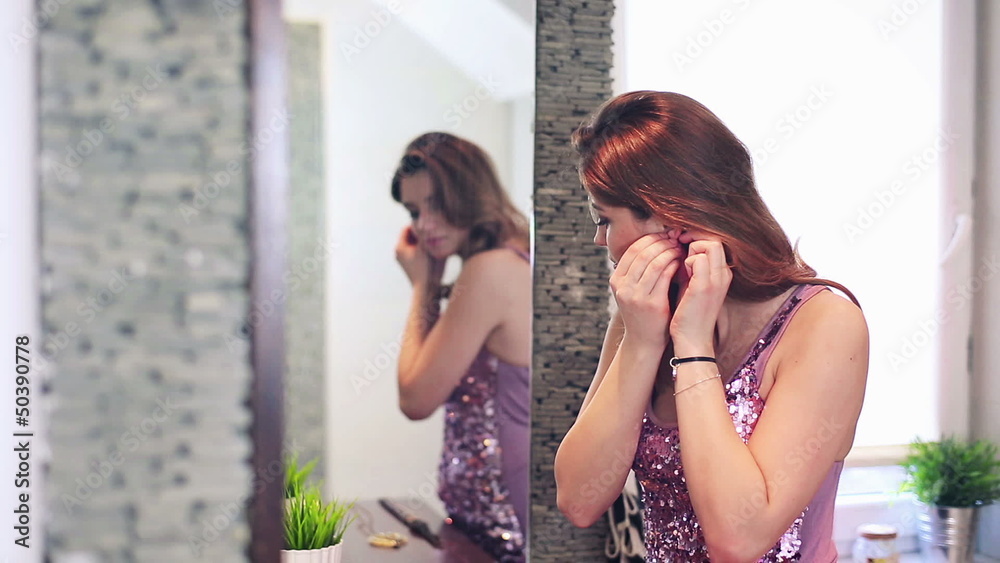 Beautiful woman putting on earrings in bathroom