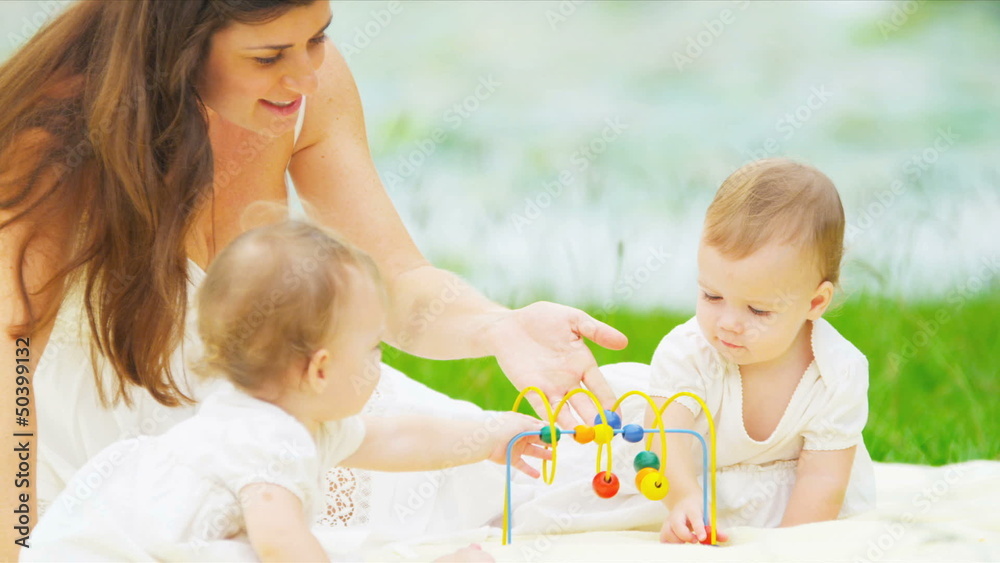 Caucasian twins and mother playing together in garden Caucasian twins and mother playing together in garden