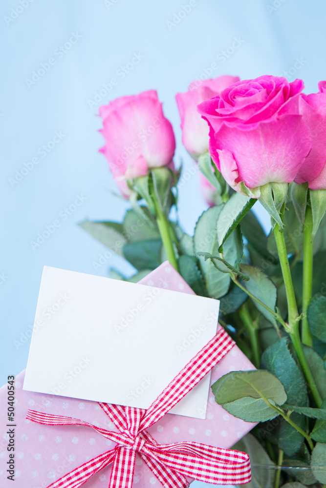 Fototapeta premium Bouquet of pink roses in vase with pink gift and blank card