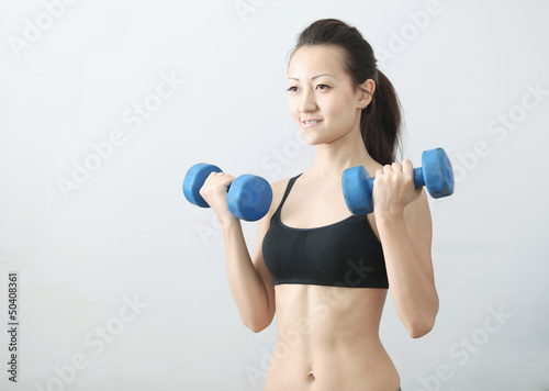 The girl in sportswear is engaged in the gym with dumbbells
