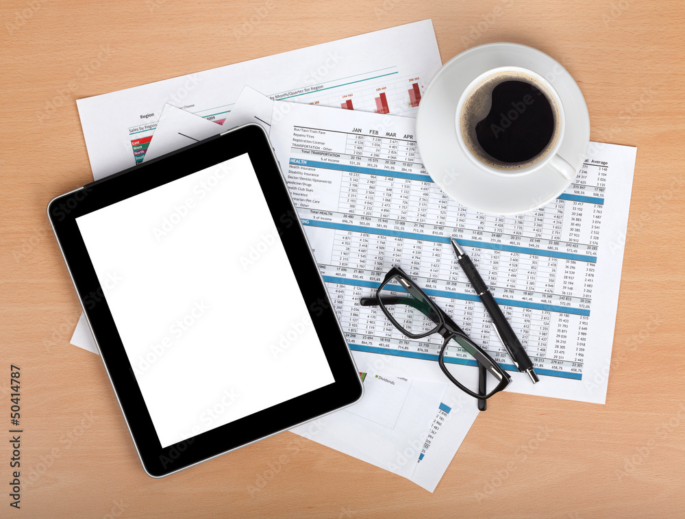 Tablet with blank screen over papers with numbers and charts Tablet with blank screen over papers with numbers and charts