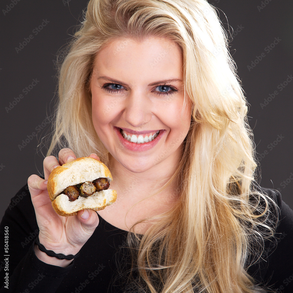 Hübsche blonde Frau zeigt Bratwurst Semmel und lacht Porträt