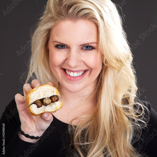 H  bsche blonde Frau zeigt Bratwurst Semmel und lacht Portr  t