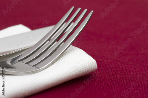 Knife and fork on folded white napkin on red tablecloth