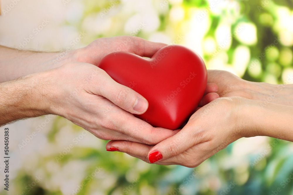 Red heart in woman and man hands, on green background Red heart in woman and man hands, on green background