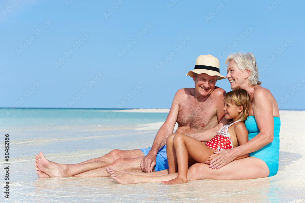Grandparents With Granddaughter Enjoying Beach Holiday